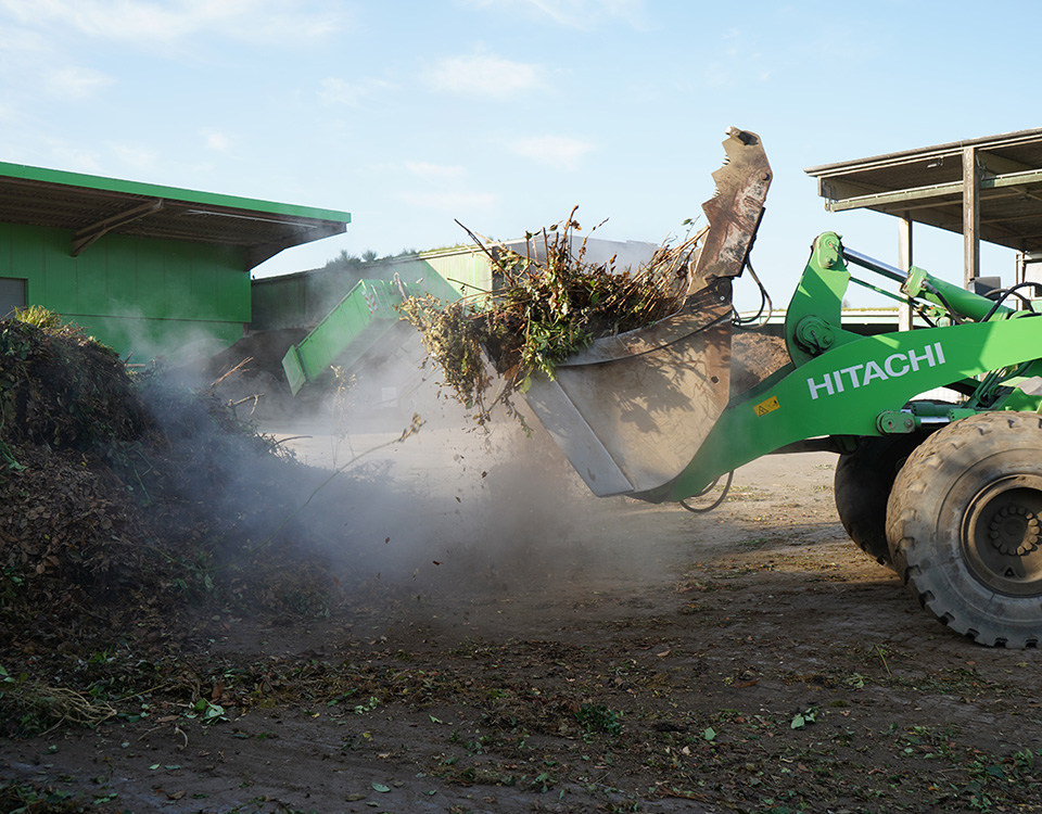 Grüner Bagger bringt Grünabfall auf Komposthaufen