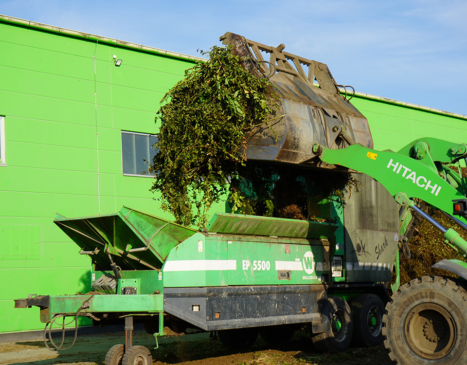 Bagger kippt Grünabfall in Siebmaschine